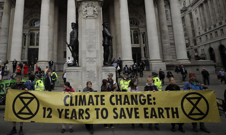 FILE - In this Thursday, April 25, 2019 file photo, Extinction Rebellion climate change protesters hold up a banner near the Bank of England, in the City of London. The environmental activist group Extinction Rebellion has postponed a plan to shut down London's Heathrow Airport with drones after it was criticized by politicians and police. The anti-climate change group said Sunday, June 16 it would "not be carrying out any actions at Heathrow Airport in June or July." (AP Photo/Matt Dunham, file)