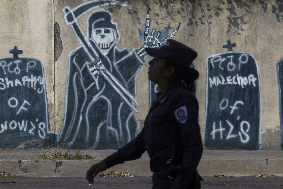 In this April 14, 2014 photo, a police officer walks past graffiti depicting gang members that have died during a patrol in a neighborhood controlled by the Mara Salvatrucha gang in Ilopango, El Salvador. Public Safety Minister Ricardo Perdomo said the gangs have also increased their attacks against police. He said members of the Mara 18 gang have orders to take revenge police and soldiers who wound or kill one of their own. (AP Photo/Salvador Melendez)