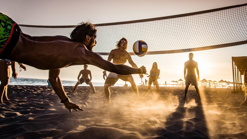 Group of young people having fun while playing beach volleyball in summer day at sunset.