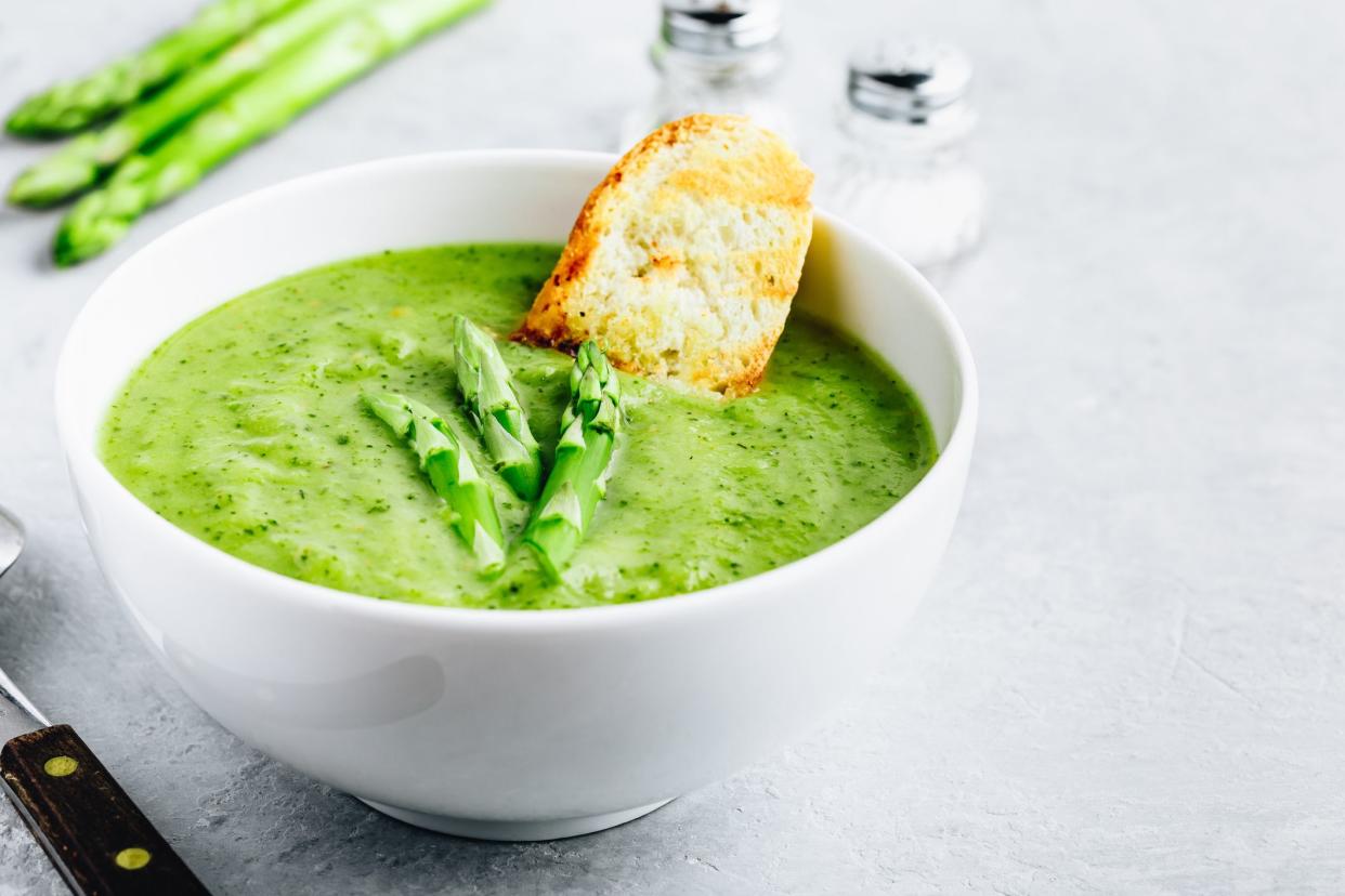 Asparagus cream soup with croutons on gray stone background. Green summer vegetable soup.