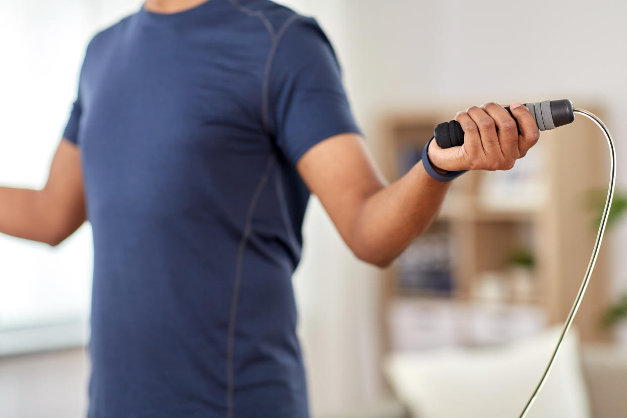 fitness, sport, exercising and healthy lifestyle concept - man skipping with jump rope at home