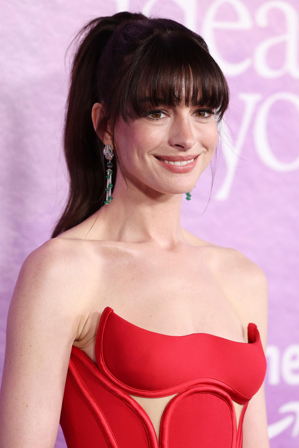 Woman with high ponytail wearing a strapless red gown and green earrings