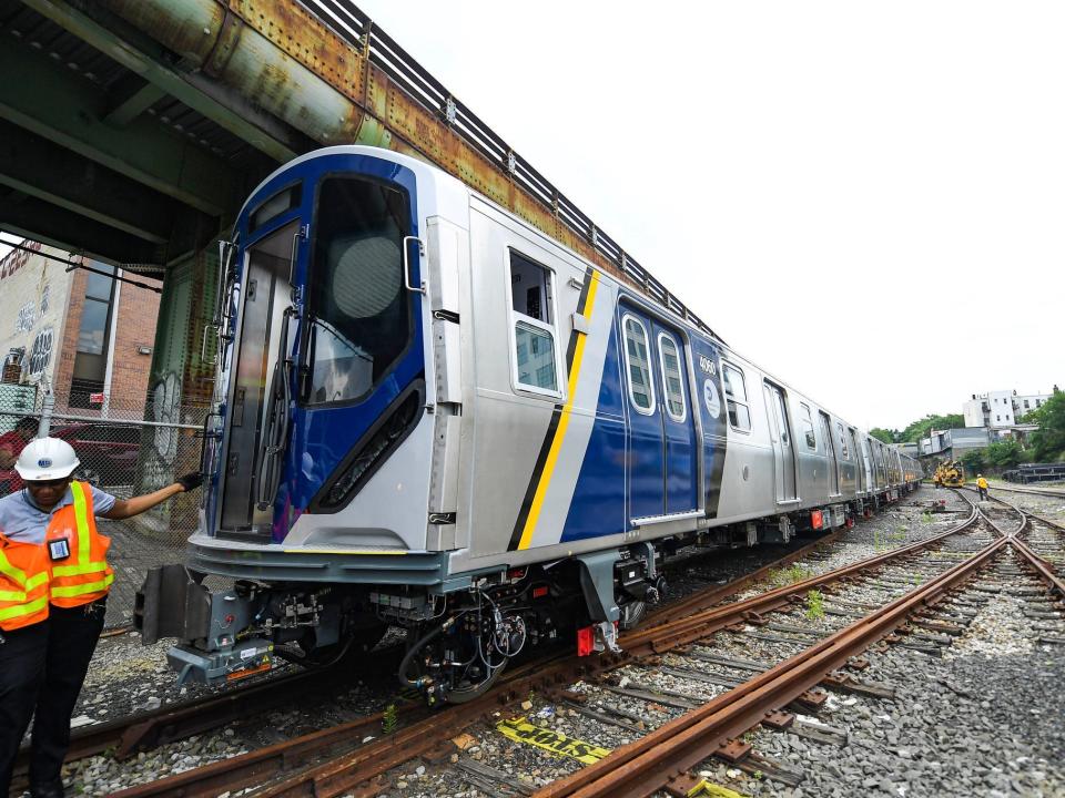 The newest subway cars are seen on a train track on the left side of the image with a worker standing in front of it.