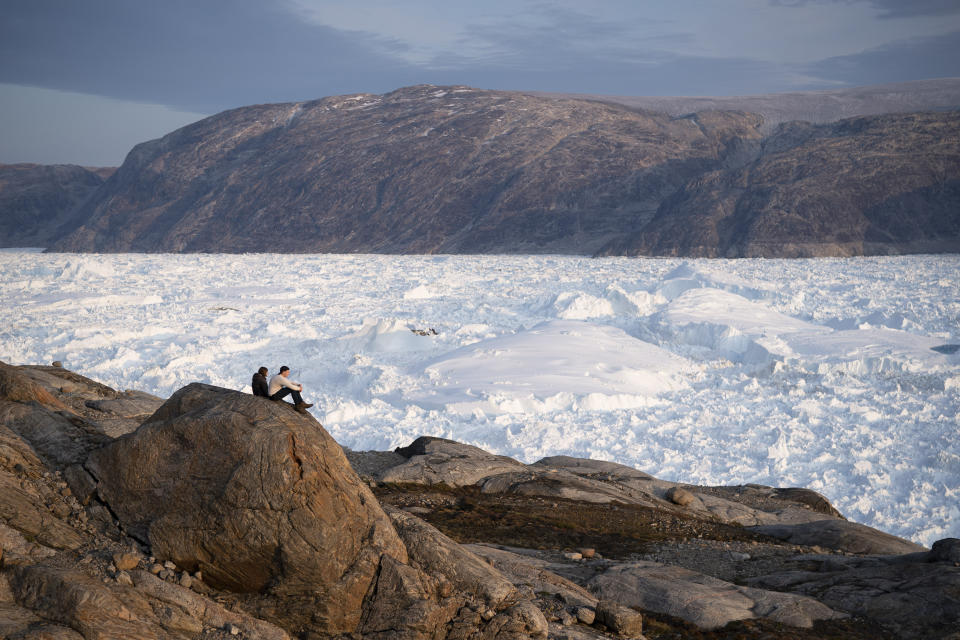 FILE - In this Aug. 16, 2019, file photo, NYU student researchers sit on top of a rock overlooking the Helheim glacier in Greenland. As warmer temperatures cause the ice to retreat the Arctic region is taking on new geopolitical and economic importance, and not just the United States hopes to stake a claim, with Russia, China and others all wanting in. (AP Photo/Felipe Dana, File)
