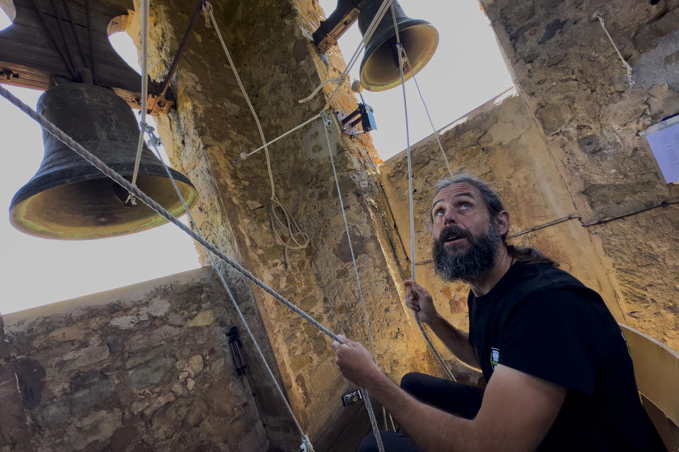 Sitting in a chair with ropes looped around both feet and hands, Joan Carles Osuna, a student of the Vall d'en Bas School of Bell Ringers, performs playing all four bronze bells at the church bell tower of the12th-century Sant Romà church, at the village of Joanetes, about two hours north of Barcelona, Spain, Saturday, July 29, 2024. A school set up to revive the manual ringing of church bells has graduated its first class of 18 students after learning their ringing skills. (AP Photo/Emilio Morenatti)