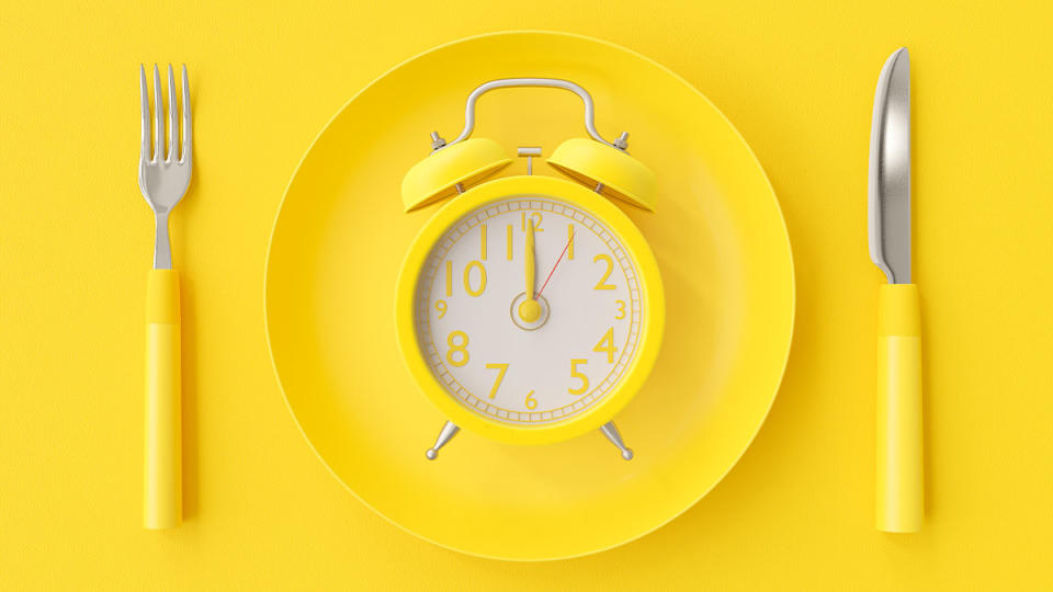 Yellow clock laid on a plate surrounded by a fork and knife 