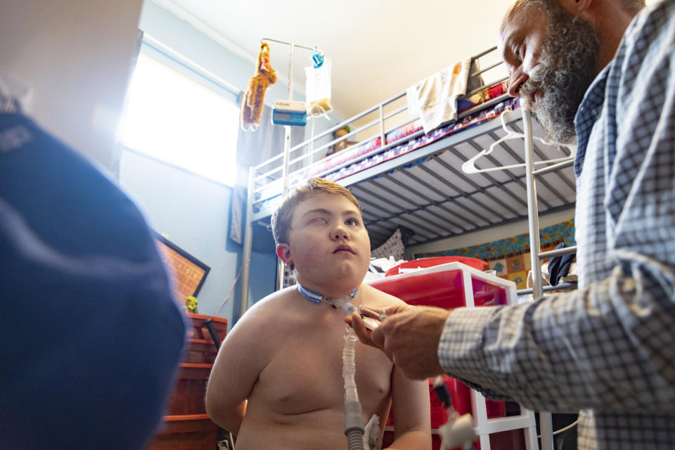 Nathan Hill changes the trach tube on his son Brady at their home in Meridian, Idaho, June 19, 2023. Brady survived a rare brain cancer as a baby, but requires round the clock care. Each morning Nate and his wife spend about 3 hours with Brady performing his medical cares and getting him ready for the day. Families of severely disabled children across the country are worried about the future of crucial Medicaid payments they started receiving to provide care during the COVID-19 pandemic. (AP Photo/Kyle Green)