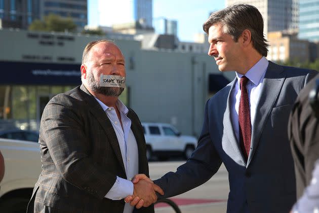 Alex Jones, shown shaking hands with his lawyer Andino Reynal, arrives at the Travis County Courthouse on July 26, 2022, with a piece of tape over his mouth that reads 