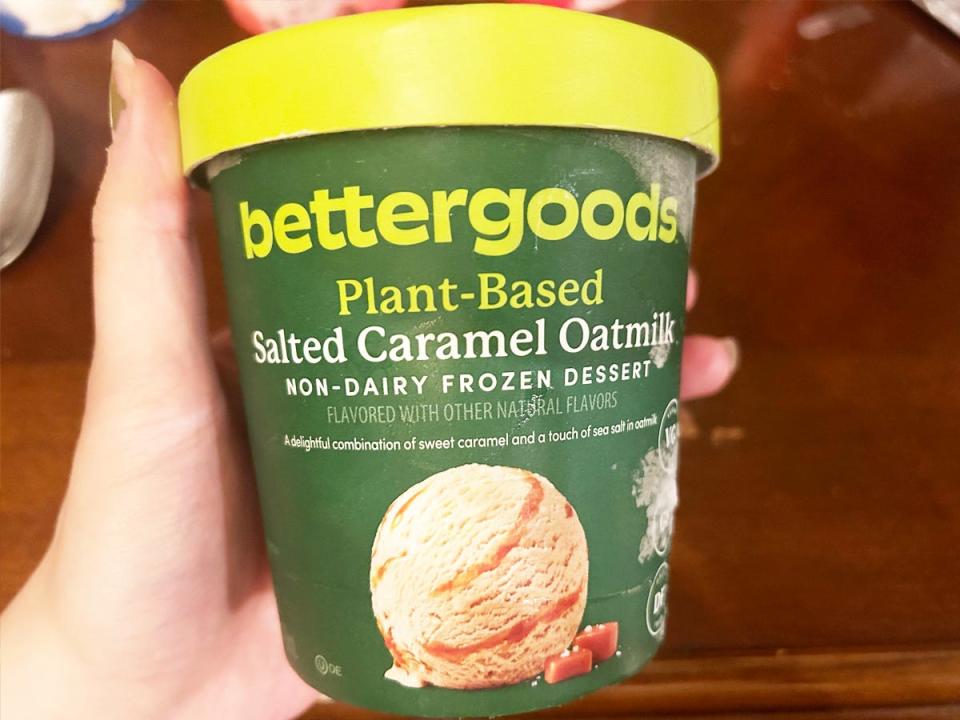A hand holds a green carton of Bettergoods salted-caramel frozen dessert with an image of a salted-caramel ice-cream scoop on the container