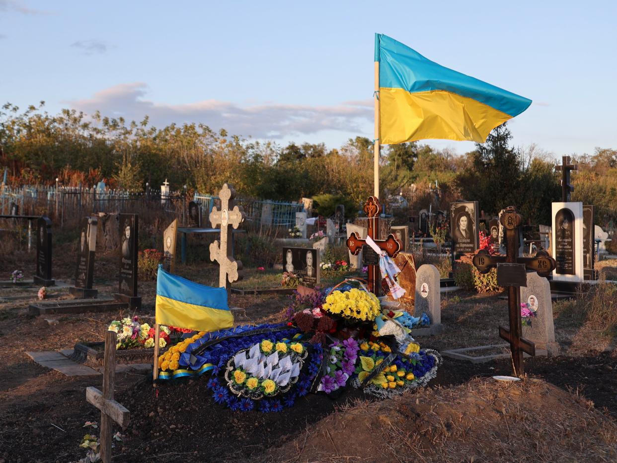 Ukrainian flags and floral tributes at the grave of fallen local soldier Andriy Kozyr, at a cemetery in Hroza (EPA)