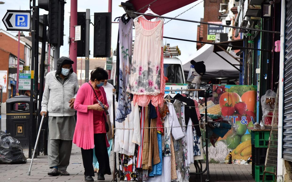 Pedestrians wearing protective face masks walk past shops in the Handsworth area of Birmingham - JUSTIN TALLIS/AFP