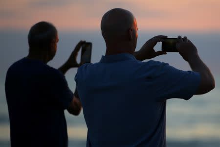 People use their mobile phones to take pictures of the setting sun while at the beach in Encinitas, California. U.S., July 5, 2017. REUTERS/Mike Blake