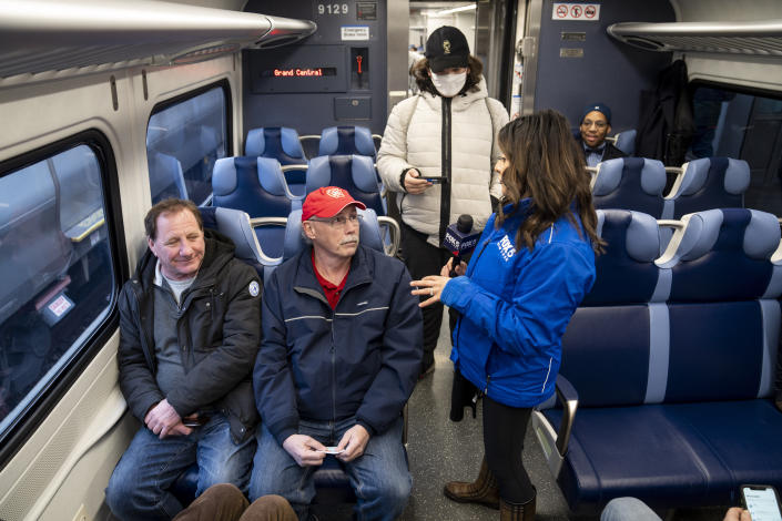 Passengers are interviewed by local reporters on a Long Island Rail Road train before it departs for its inaugural trip from Jamaica station towards Grand Central Station, Wednesday, Jan. 25, 2023, in the Queens borough of New York. After years of delays and massive cost overruns, the railway project has begun shuttling its first passengers between Long Island to the latest addition to New York City's iconic Grand Central Terminal, dubbed Grand Central Madison because of its location along Madison Avenue. (AP Photo/John Minchillo)