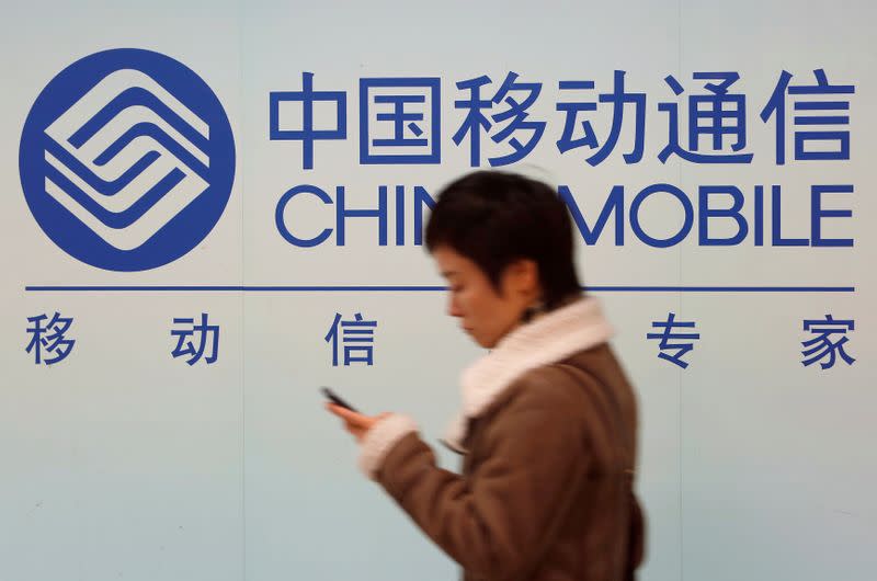 FILE PHOTO: A woman looks at the screen of her mobile phone while walking past a China Mobile sign in downtown Shanghai