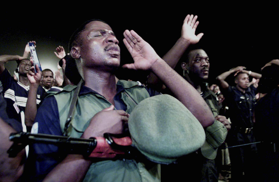 FILE - In this Dec. 5, 2001, file photo, a policeman, with his weapon slung over his chest, prays with Reinhard Bonnke for the healing of his physical ailment during the "Great Gospel Crusade," in Osogbo, Nigeria. Bonnke, a Pentecostal preacher whose crusades across Africa drew millions with the promise of faith healings, died Dec. 7, 2019, the ministry he founded announced. He was 79. (AP Photo/Christine Nesbitt, File)