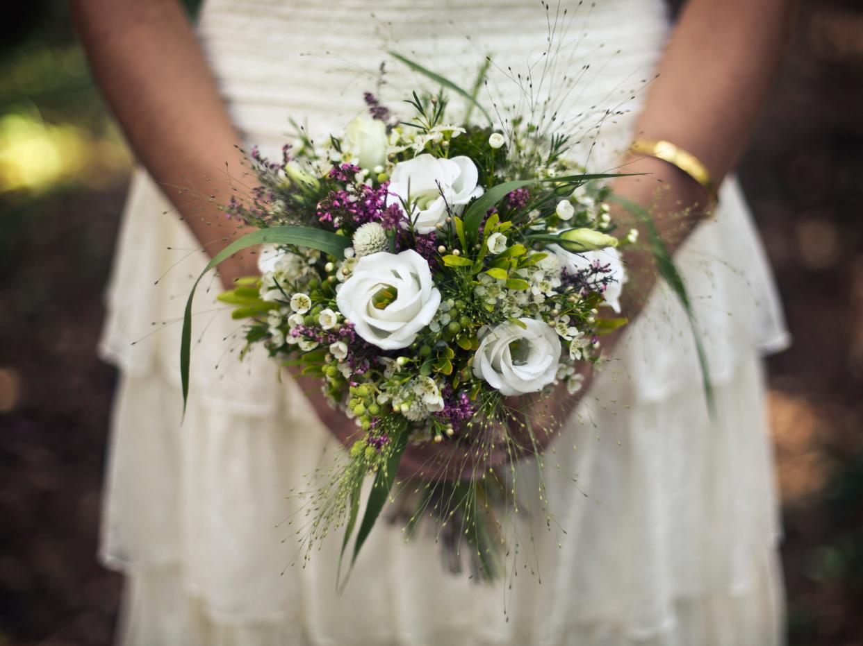 Bride holding bouquet of white and purple flowers.