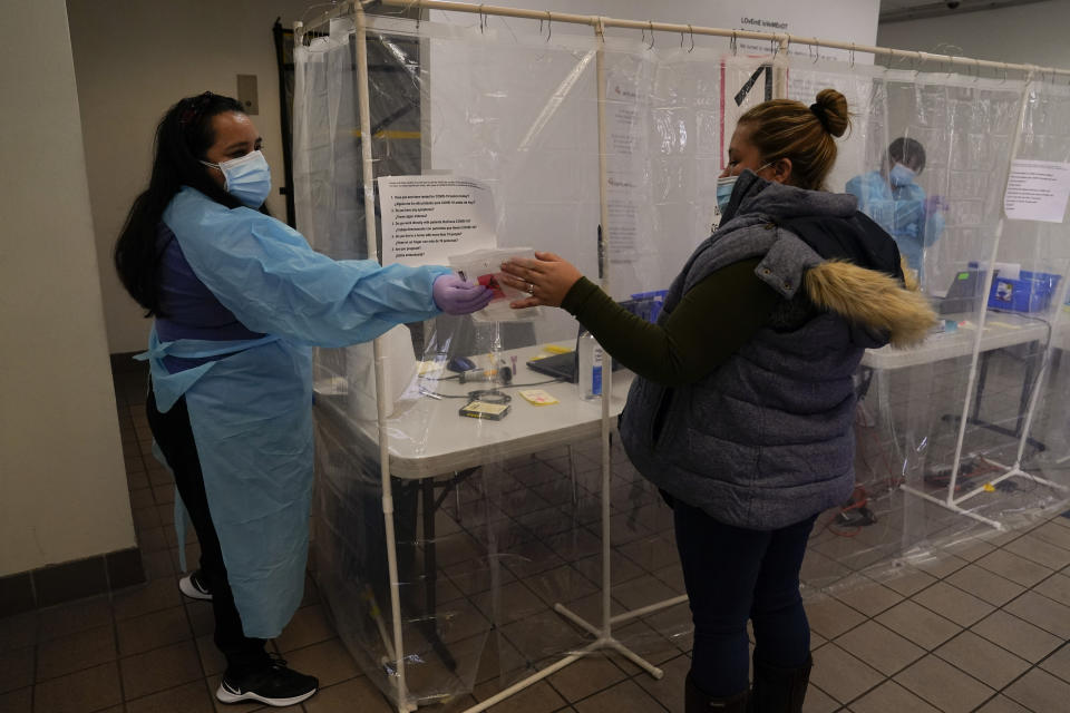 Administrative worker Veronica Esparza, right, hands a COVID-19 testing kit to a woman at a testing site in Los Angeles, Sunday, Dec. 27, 2020. Hospitals in central and Southern California are quickly running out of intensive care unit beds for coronavirus patients and state officials are poised to extend the strictest stay-at-home orders there as conditions worsen before the post-holiday surge hits. (AP Photo/Jae C. Hong)