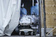 FILE - In this April 6, 2020, file photo, medical workers wearing personal protective equipment intake bodies through a tent before loading them onto a refrigerated trailer serving as a makeshift morgue at Wyckoff Heights Medical Center, in the Brooklyn borough of New York. (AP Photo/John Minchillo, File)