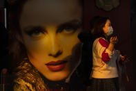 A woman wearing a face mask to protect against the spread of the coronavirus walks past a billboard at an outdoor shopping area in Beijing, Saturday, Feb. 20, 2021. China has been regularly reporting no locally transmitted cases of COVID-19 as it works to maintain control of the pandemic within its borders. (AP Photo/Mark Schiefelbein)