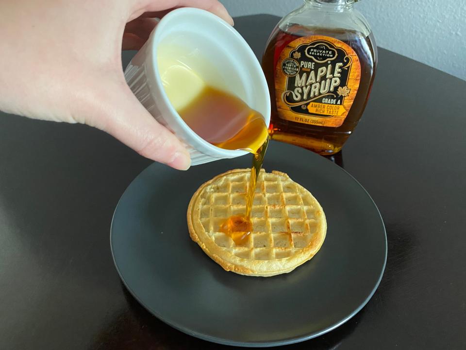 hand pouring white ramekin of real maple syrup from kroger over a frozen waffle