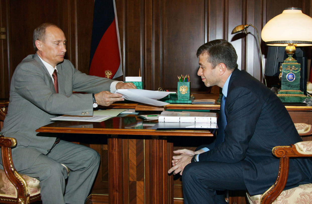 Russian President Vladimir Putin and Roman Abramovich sit across from each other at a desk during a meeting.