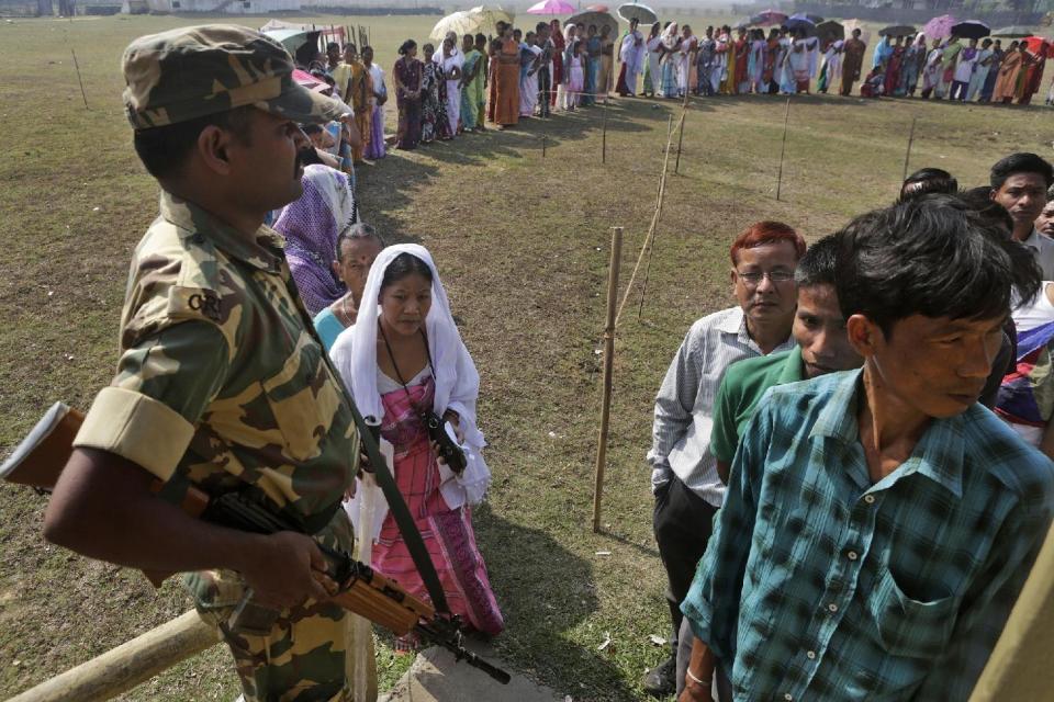 A security person stands guard as Indians wait in a queue to cast their votes during the sixth phase of polling of the Indian parliamentary elections in Sonapur village, outskirts of Gauhati, India, Thursday, April 24, 2014.The multiphase voting across the country runs until May 12, with results for the 543-seat lower house of parliament expected on May 16. (AP Photo/Anupam Nath)