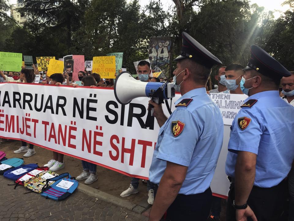 A police officer uses a loudspeaker asking protesters to end the rally in Tirana, Albania, Monday, Sept. 14, 2020. Scores of family members of 52 children who have remained in Syria after their parents joined Islamic terror groups gathered in front of the main government building shouting for help, calling on the government to keep the pledge to bring their children back. (AP Photo/Llazar Semini)