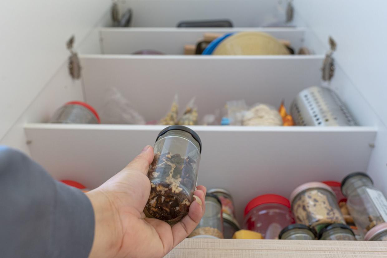 Low angle view of a human hand holding a bottle of raw food from a shelf in a cabinet in the kitchen pantry