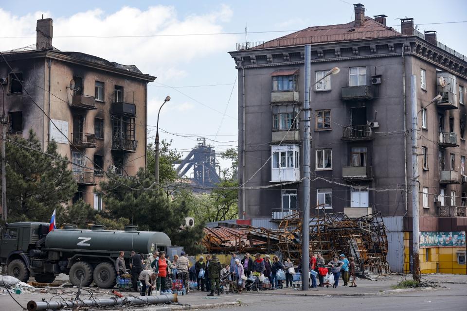 Local civilians gather to receive pure water distributed by Russian Emergency Situations Ministry in Mariupol, in territory under the government of the Donetsk People's Republic, eastern Ukraine, Friday, May 27, 2022, with the Illich Iron & Steel Works Metallurgical Plant is in the background. (AP Photo/Alexei Alexandrov)