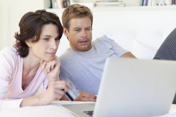 40-something couple lounging side by side while browsing on a laptop
