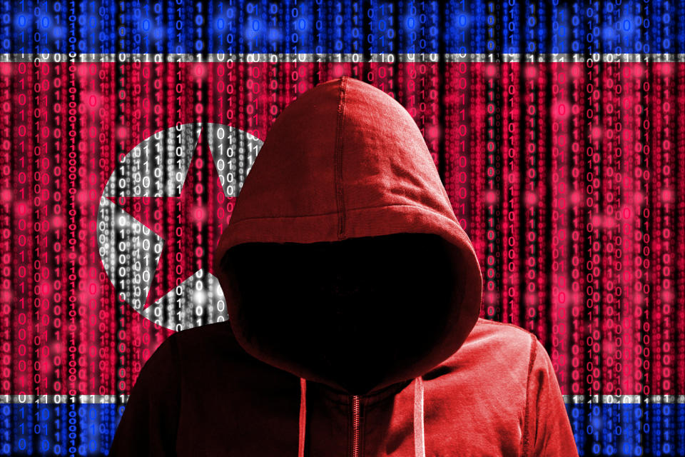 Hacker in a dark red hoody in front of a digital korean flag and binary streams background cybersecurity concept