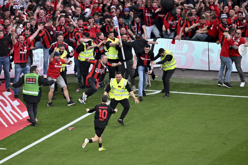 Leverkusen's Florian Wirtz calms down fans and security personnel as he celebrates after scoring his side's fourth goal of the game during the Bundesliga soccer match between Bayer Leverkusen and Werder Bremen at the BayArena in Leverkusen, Germany, Sunday April 14, 2024. (David Inderlied/dpa via AP)