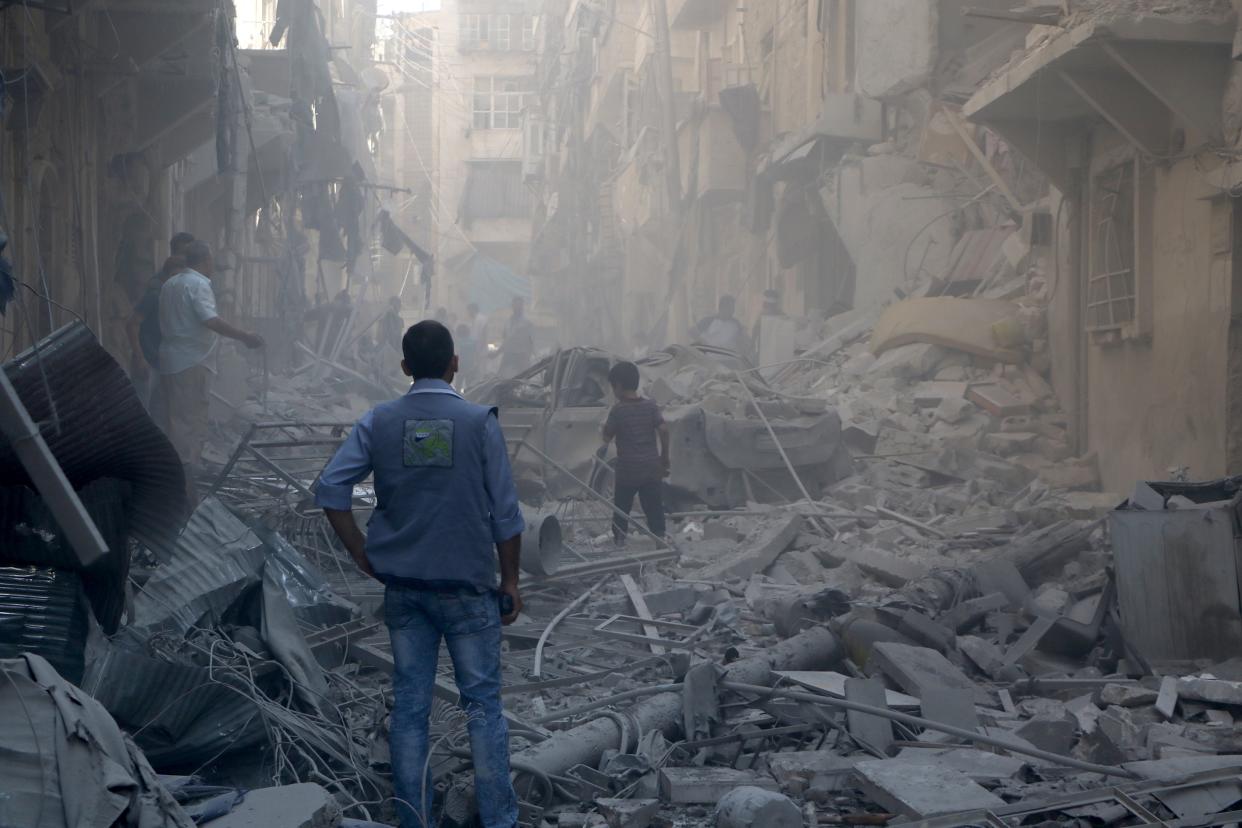 People stand amid the wreckage of collapsed buildings after Syrian army war planes staged airstrikes with vacuum bombs.