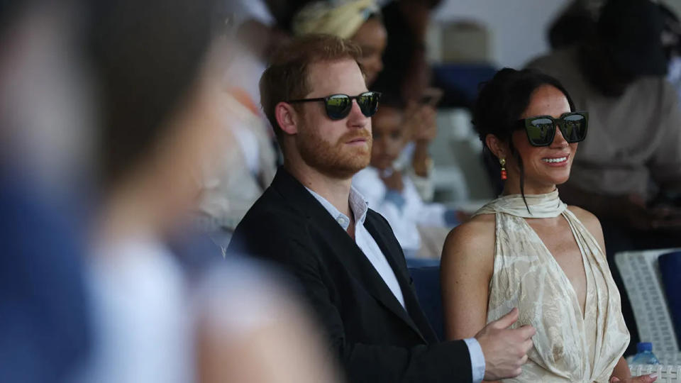 Prince Harry and Meghan Markle sitting together and wearing sunglasses