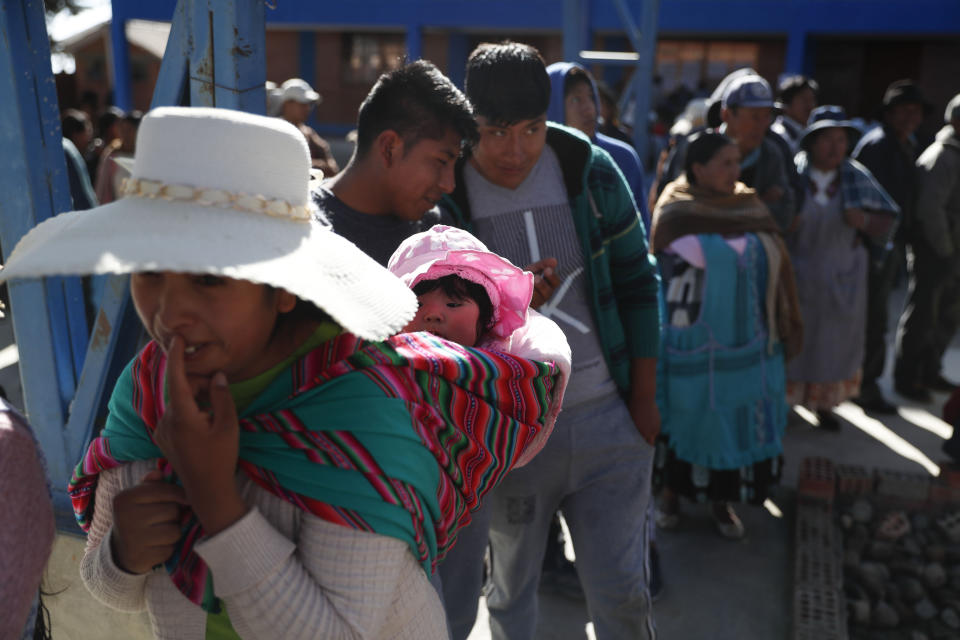 A woman carries her child on her back as she stands in line to vote at a polling station during general elections in La Paz outskirts, Bolivia, Sunday, Oct. 20, 2019. Bolivians are voting in general elections Sunday where President Evo Morales is Presidential candidate for a fourth term. (AP Photo/Jorge Saenz)