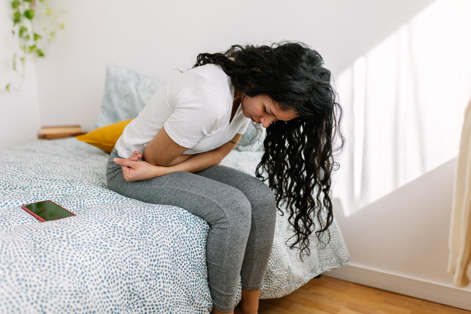Young millennial woman suffering with stomach pain, feeling unwell sitting on bed in the morning. HG is most likely related to changes in hormone levels in pregnant people. (Getty)