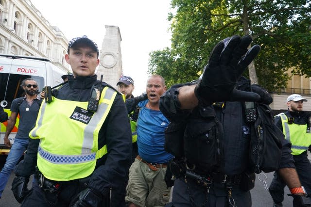 Police officers escort a demonstrator, wearing blue T-shirt and khaki shorts, past the cenotaph during a demonstration on Whitehall.