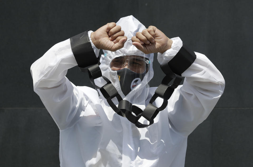A protester dressed in a protective suit with hands tied with mock chains hold a rally against the G7 summit outside the British Embassy in Taguig, Philippines on Friday, June 11, 2021. The group called on G7 Summit member nations for debt cancellation for poor countries facing difficulties due to the COVID-19 pandemic. (AP Photo/Aaron Favila)