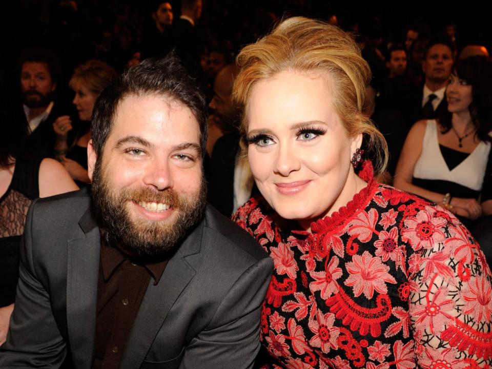Simon smiling in a suit and Adele smiling leaning into him in a red floral dress.