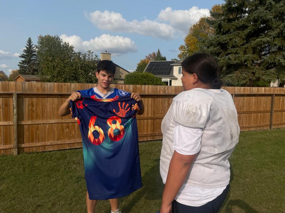 A teammate holds up the special reconciliation jersey for Rocco Linklater, right, to see for the first time.