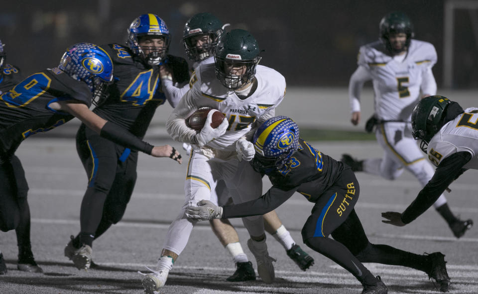 Paradise running back Tyler Harrison, center, is tackled by Sutter Union cornerback Roman Resendez during the first half of a Northern Section Division III high school football playoff game Saturday, Nov. 30, 2019, in Yuba City, Calif. Paradise had an undefeated season and made it to the section championship game a year after the deadliest wildfire in California history that killed dozens and destroyed nearly 19,000 buildings including the homes of most of the players. (AP Photo/Rich Pedroncelli)