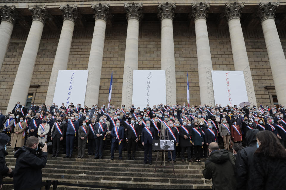 French lawmakers listen to the national anthem to pay tribute to slain teacher Samuel Paty, Tuesday, Oct.20, 2020 on the steps of the National Assembly in Paris. A memorial march will be held Tuesday evening near Paris in homage to the history teacher who was beheaded last week, while French police said 16 people remain in custody as part of the investigation into the attack. (AP Photo/Lewis Joly)