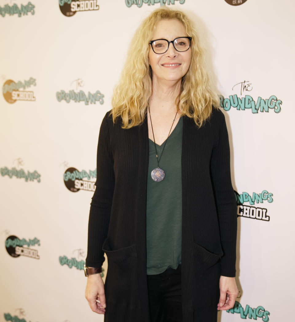 Close-up of Lisa smiling in glasses, a long jacket, and a shirt at a media event