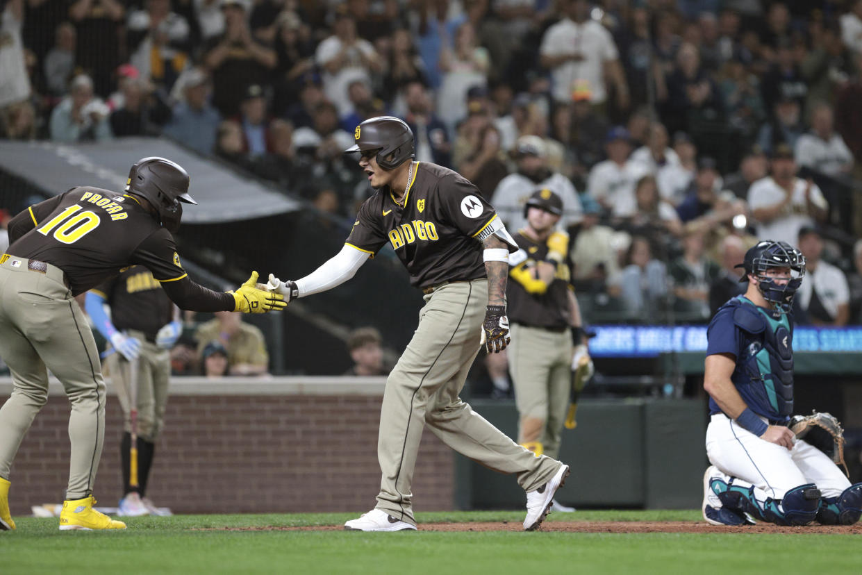 San Diego Padres' Manny Machado, center, celebrates with Jurickson Profar, left, after they scored on Machado's two-run home run as Seattle Mariners catcher Cal Raleigh, right, looks on during the sixth inning of a baseball game, Tuesday, Sept. 10, 2024, in Seattle. (AP Photo/Jason Redmond)