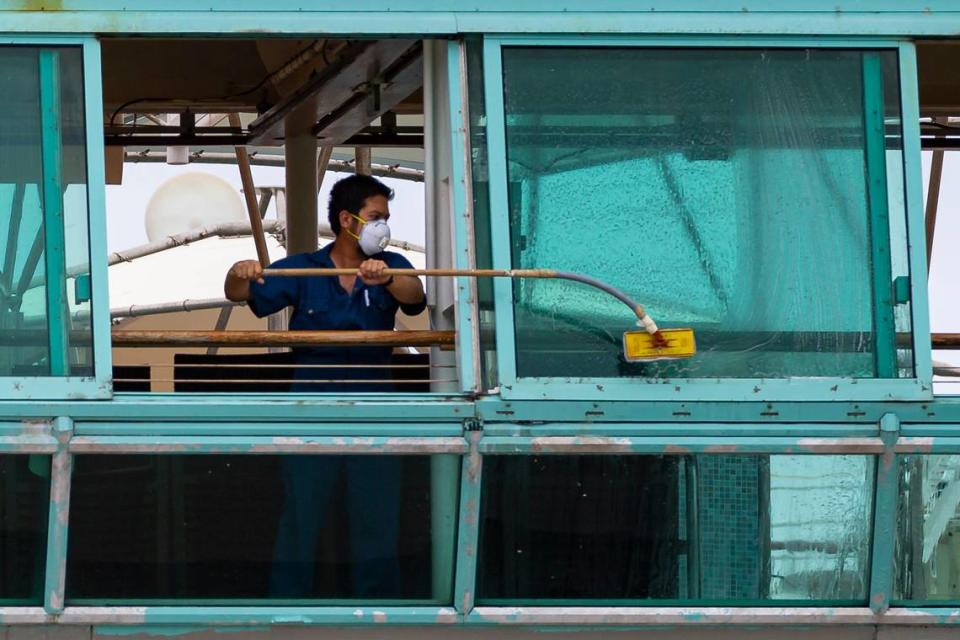 A crew member aboard Royal Caribbean’s Vision of the Seas cruise ship cleans the window as the ship is docked at PortMiami on Friday, May 15, 2020, in Miami, Florida.