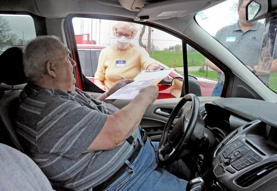 Ed Snell is given his ballot by poll workers Mary Starn and Chad Haston at Schmid Hall in Orrville so he could vote from his car Tuesday morning.