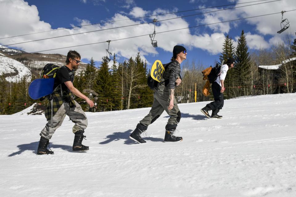 This Tuesday, March 24, 2020 photo shows snowboarders, from left, Colin Tabb, Tyler Alvarez and Shaun Carroll, determined to get in a run, hike up an empty ski run past a closed chair lift at Vail, Colo., after Vail Ski Resort closed for the season amid the COVID-19 pandemic. “Today it’s desolate. It’s a ghost town," said Tabb, a Vail resident and snowboarder. “Usually we are fighting lift lines and we are doing our thing still, but it’s a complete ghost town.” (AP Photo/Michael Ciaglo)