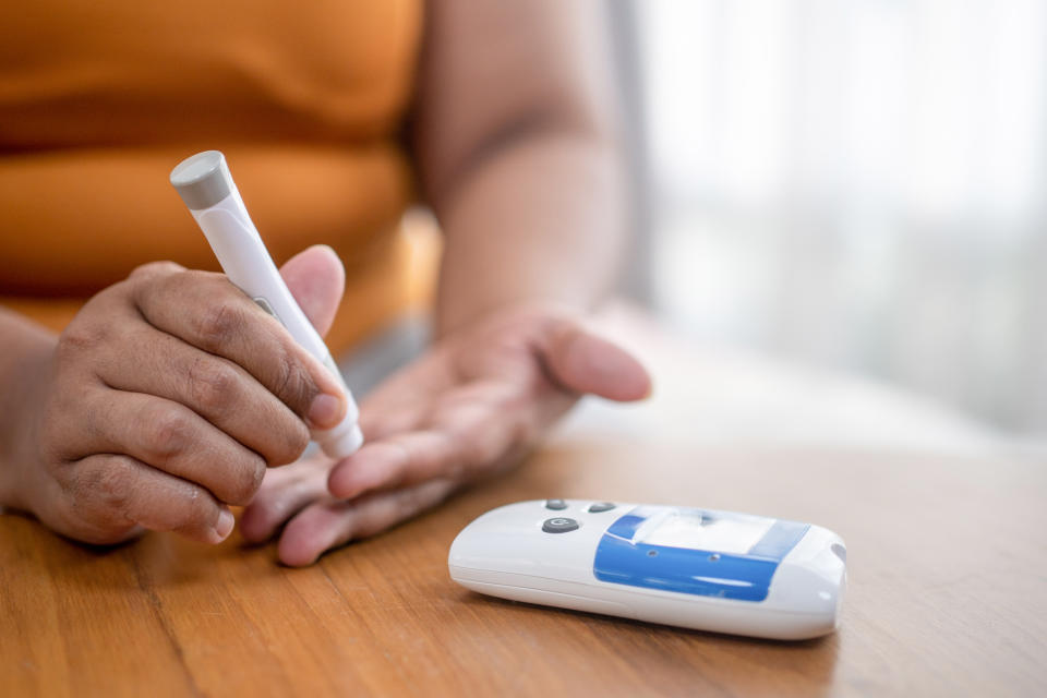 A person uses a lancet device to prick their finger for a blood sugar test, with a glucose meter on the table