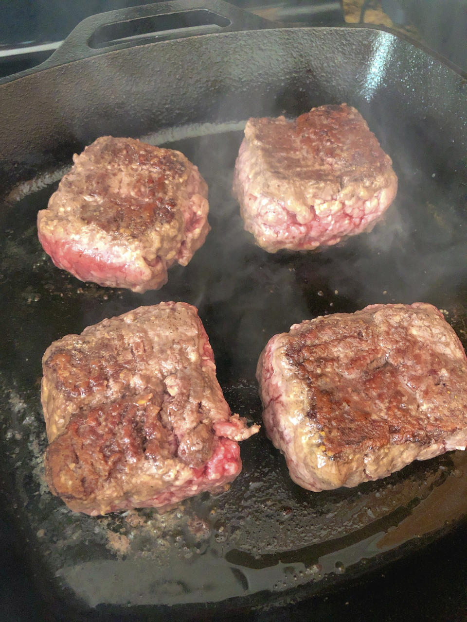 This June 2020 photo shows beef patties frying in a cast iron pan in Alexandria, Va. To get the best tasting burger, try making your own blend with better quality cuts of beef. (Elizabeth Karmel via AP)