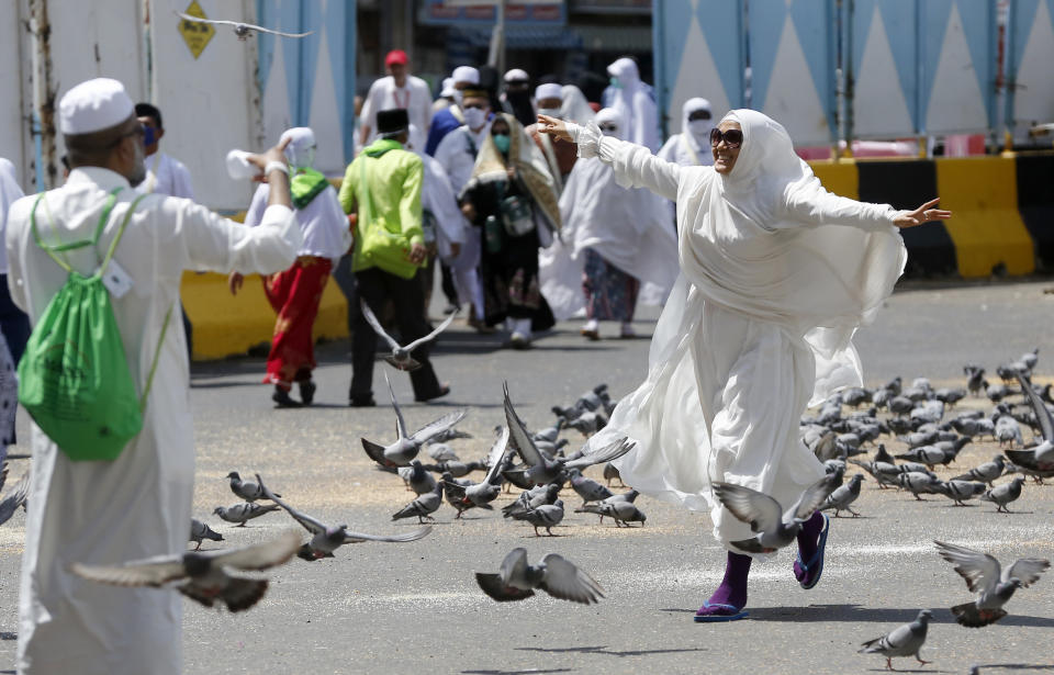 FILE - In this Sunday, Aug. 4, 2019 file photo, a Moroccan pilgrim runs as pigeons fly outside the Grand Mosque in the Muslim holy city of Mecca, Saudi Arabia. The hajj is a pillar of Islam, required of all Muslims once in a lifetime. It is a physically demanding journey that Muslims believe offers a chance to wipe clean past sins and start anew before God. Pilgrims seek to deepen their faith on the hajj, with some women adopting the head covering known as the "hijab.” (AP Photo/Amr Nabil, File)